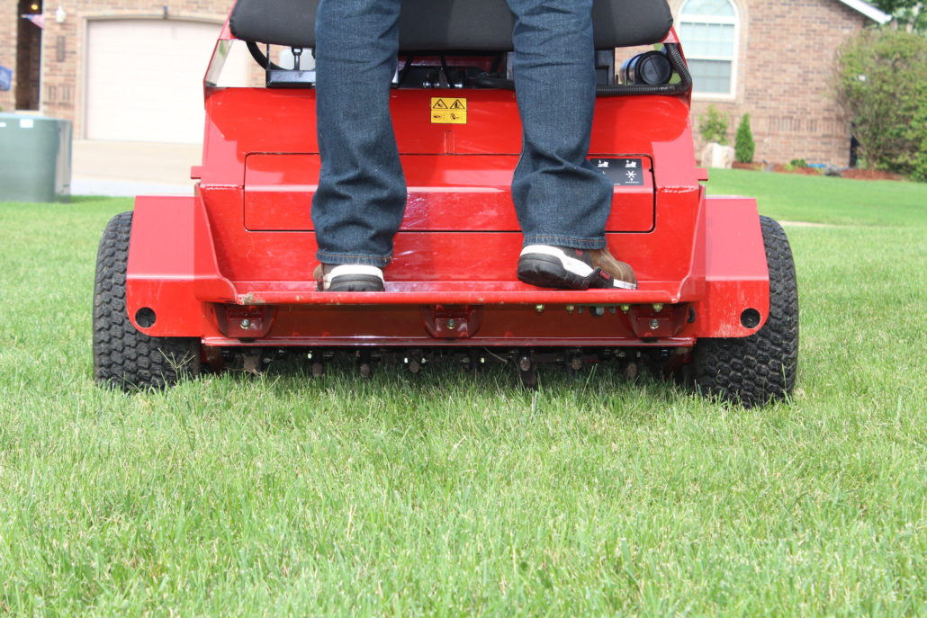 A PURE Lawn employee standing on a lawn aeration machine pulling plugs out of the lawn.