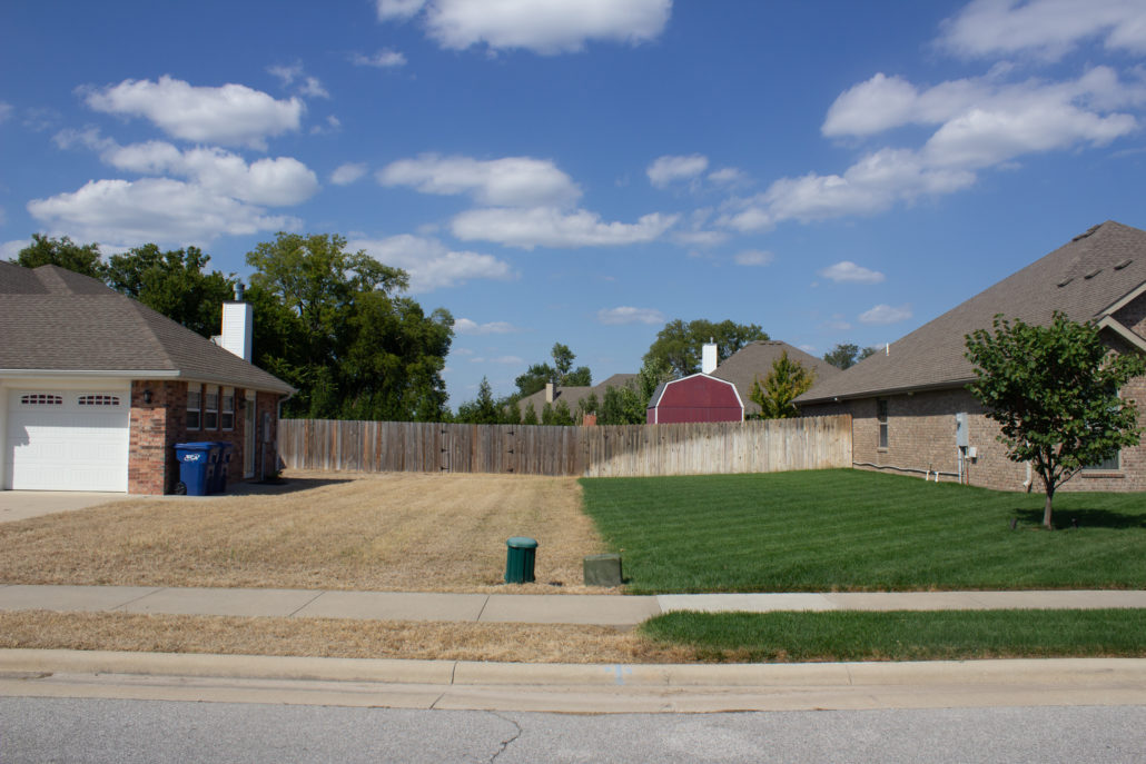 A photo of 2 neighbors lawns side by side. One was renovated by PURE Lawn Management and is green and beautiful. The other neighbors lawn in brown and dead and will be renovated also by PURE Lawn Management.